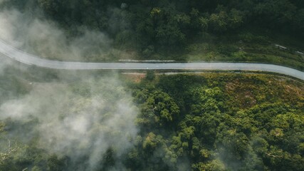 Aerial view of a winding road surrounded by a lush green landscape with trees in the distance.