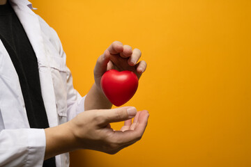 Doctor hand holding red heart on yellow background Cardiology, medicine, donation and healthcare concept