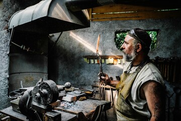 Blacksmith using a large knife to craft an interesting object in his workshop