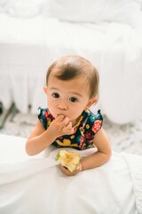 Adorable Chinese baby girl in floral dress eating apple with finger in mouth