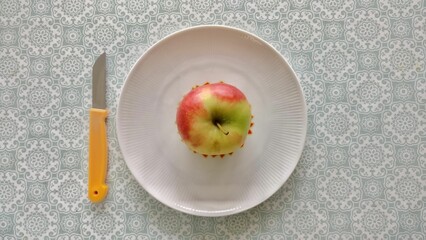 Ripe, red apple atop a white plate, with a stainless steel knife placed beside it
