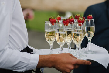 The waiter serves and carries a tray with glasses of champagne and strawberries. Party and holiday...