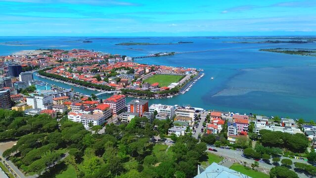 Aerial view of the old city. Roofs of buildings with red tiles and many chimneys. The bell tower of the Catholic Cathedral in the city center. Traveling through narrow streets. Italy Grado 09.2023