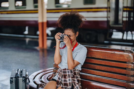 Asian teenage girl african american traveling using a camera take a photo to capture memories while waiting for a train at the station.