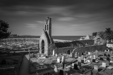 Ancient cemetery with a clock tower and multiple tombstones in grayscale in Howth, Dublin, Ireland