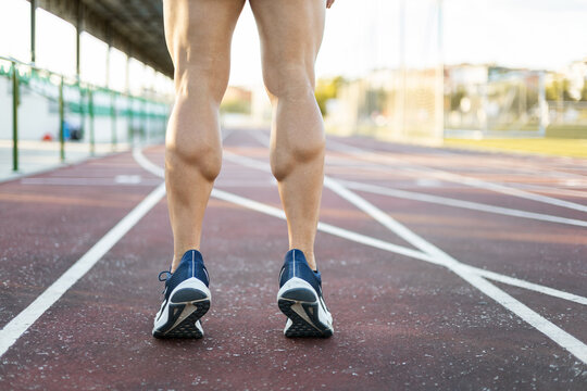 Photo of muscular legs of an unrecognizable athlete posing on an outdoor running track on tiptoe. Concept of running, exercise on an athletics track. Copyspace.