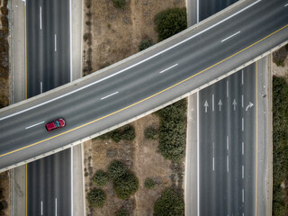 A top down view from a drone of a red car driving on an interchange 