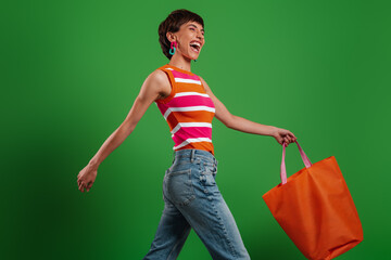Happy young woman carrying shopping bag while walking against green background