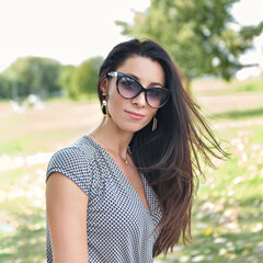 Portrait of a beautiful young brunette woman in sunglasses in the park
