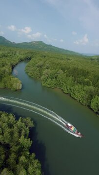 Vertical video. Asian traditional longtail rasta boat tourist people floating narrow strait amazon river lush trees aerial view. FPV sport drone water transport pond surface tropical mountain valley