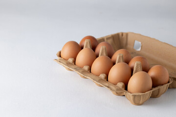 A dozen eggs with brown shells in a cardboard box on a white background. Close-up, empty space