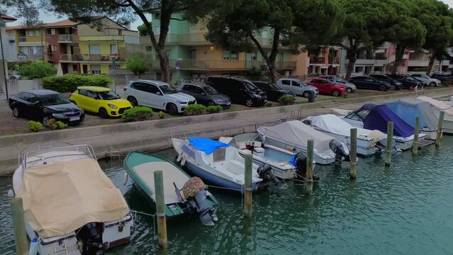 Aerial view of the sea water canal in the city center where fishing boats and amateur sailing yachts are moored. Small classic fishing boats with nets. Little Venice. Grado Italy 07.2023