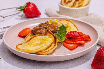 Cottage cheese pancakes, syrniki, curd fritters with strawberry, mint and powdered sugar on plate