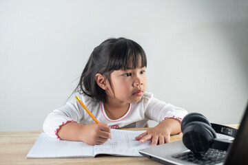 4-5 years old Asian girl wearing white shirt is studying online via computer using bluetooth...