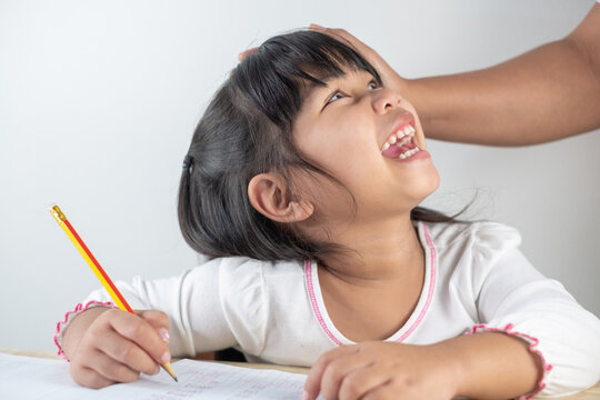 Asian girls aged 4-5 are having mom help with homework, kids holding pencils and writing homework.