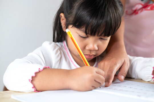 Asian girls aged 4-5 are having mom help with homework, kids holding pencils and writing homework.