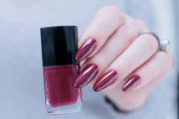 Woman hand with long nails and a bottle of dark red burgundy nail polish