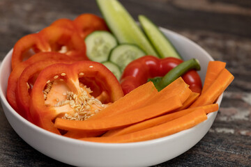 Chopped vegetables, cucumbers, paprika, carrots in a white bowl on a wooden table