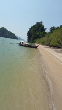 Vertical video. Flying over sand beach sea ocean tourist man running on seashore diving longtail rasta boat aerial dynamic view. FPV sport drone shot paradise island Asian seascape mountain rock cliff
