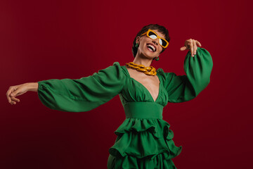 Happy young short hair woman in elegant dress dancing against red background