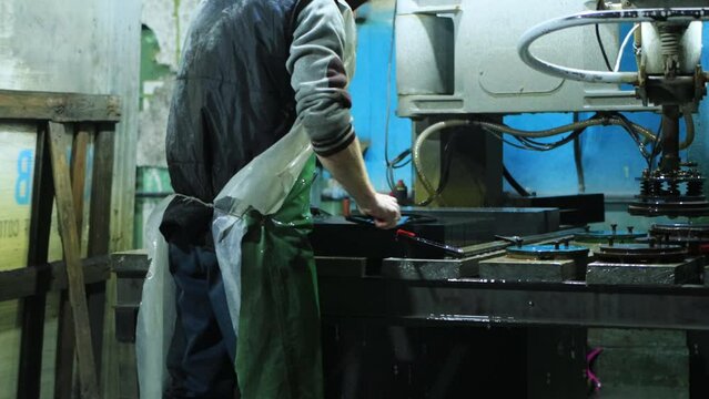 A factory worker grinds a porcelain stoneware slab with a special nozzle on a machine. Production for the production of large-format glossy granite for interior decoration, industry