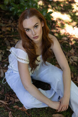 Obraz premium very pretty freckled white woman with long red hair sitting in park full of green leaves
