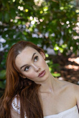 Naklejka premium very pretty freckled white woman with long red hair sitting in the park thinking and looking at the sky