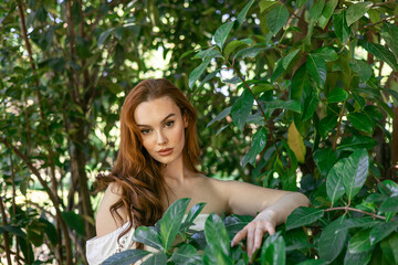 Fototapeta premium very beautiful freckled white woman with long red hair among the bushes of green leaves