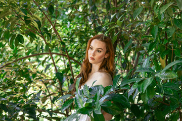 very beautiful freckled white woman with long red hair among the bushes of green leaves