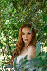 very beautiful freckled white woman with long red hair among the bushes of green leaves