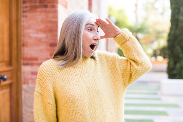 senior retired pretty white hair woman looking bewildered and astonished, with hand over forehead looking far away, watching or searching