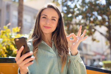 pretty woman feeling happy, showing approval with okay gesture. smartphone concept