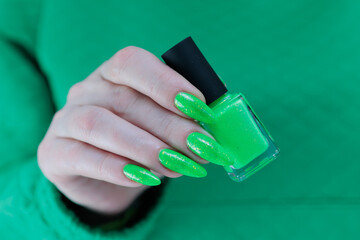 Female hand with long nails and neon green manicure with bottles of nail polish