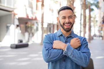 young handsome man smiling cheerfully and celebrating, with fists clenched and arms crossed, feeling happy and positive