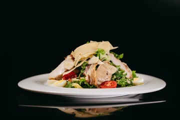 Caesar salad with chicken and cheese on a black background