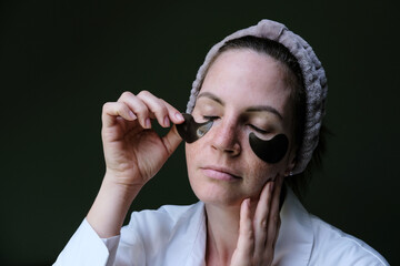A young woman applies moisturizing patches under her eyes. Home cosmetic procedures.