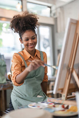 Professional African American female artist painting on canvas in studio. Woman painter painting at an painting studio