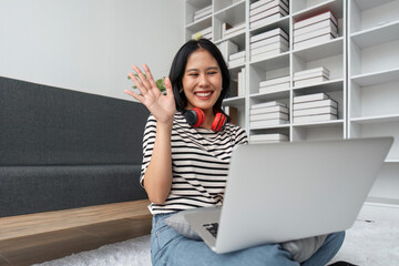 Portrait of happy attractive asian woman and having video call, waving hand at laptop, having online meeting or conversation while relaxing at home