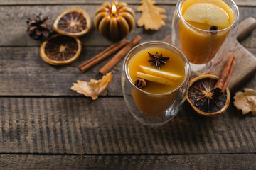 Obraz na płótnie Canvas Autumn beverage in two glasses on wooden table background. Autumn warm cocktail with autumn fall leaves, cinnamon sticks and candle. Top view