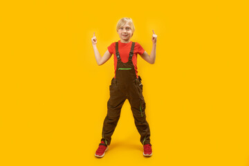 Fototapeta na wymiar Caucasian teenage boy in work jumpsuit stands with his legs spread wide and points his index finger up. Copy space.