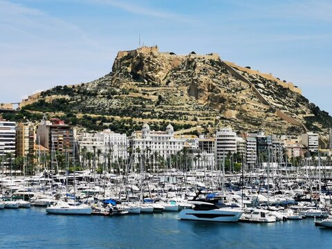imagen de Alicante desde el mar en primer lugar el puerto detrás la sky line de los edificios de alicante y al fondo el castillo de Santa barbara 