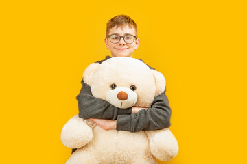 Smiling bespectacled brunett boy holds large teddy bear toy looking into the camera. Copy space, mock up.