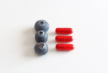 Three blueberries next to 3 capsules or medicines.