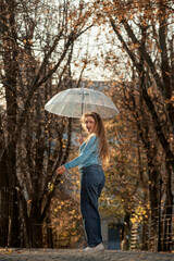 Beautiful girl in blue sweater with transparent umbrella on autumn alley. Young woman in autumn park
