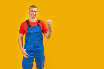 Smiling male foreman engineer wearing blue overalls and points with his finger to the side. Yellow...