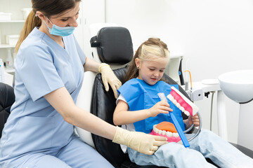 Little child in dentists surgery learning how to brush teeth with giant toothbrush