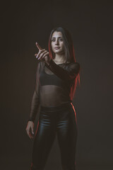 Naklejka premium Portrait of beautiful cyber model woman posing wearing black leather leggings outfit with neon glow fluorescent led light in a black background typing in the air