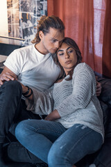 Obraz premium Inside house couple shooting sitting on sofa relaxing and looking outside the frame - Yellow and blue atmosphere tone light. Lovers shot in house studio with red courtain