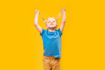 Portrait of smiling little girl having fun and holding two ponytails with her blonde hair. Yellow...