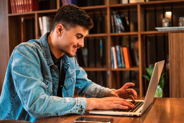 A happy male college student using a laptop in a university library.